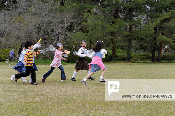Japanische Kinder laufen hinter Seifenblasen her im Botanischen Garten  Kyoto  Japan  Asien