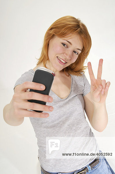Attractive  red-headed woman taking a picture with a mobile phone  doing a peace sign