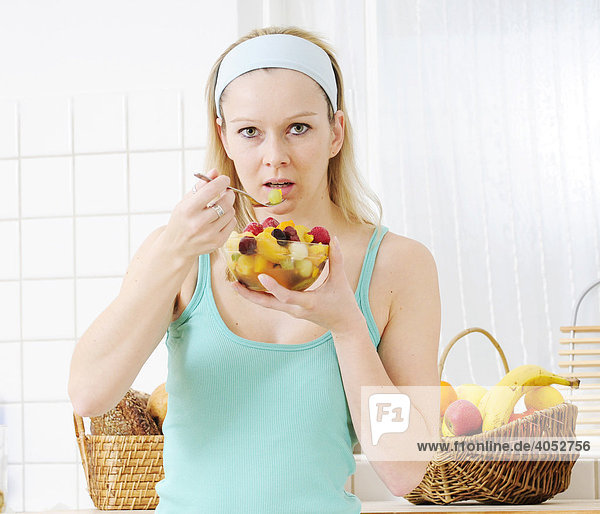 Junge blonde Frau isst Obstsalat aus einer Schüssel
