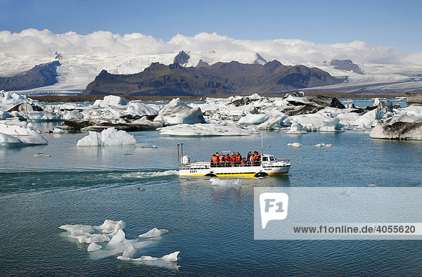 In the Joekulsarlon glacier lagoon of the Vatnajoekull Glacier  people travelling in an boat between the floating icebergs  which are partly coloured by black lava ash  Iceland  Europe
