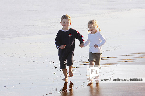Boy  4 years  and girl  3 years  jumping and running hand in hand on the beach of Fuerteventura  Canary Island  Spain  Europe