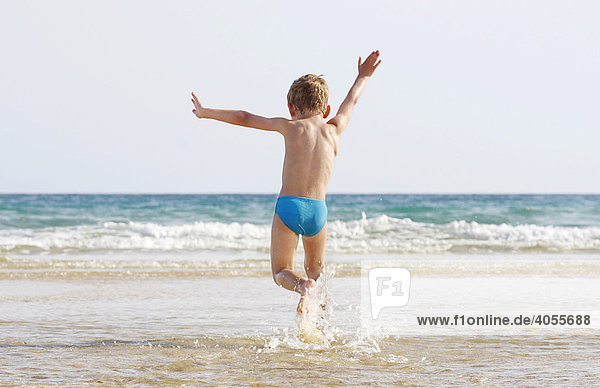 Boy  4 years  jumping and running in the small waves on the beach of Fuerteventura with delight  Canary Island  Spain  Europe