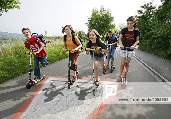 Schulkinder  Jungen und Mädchen  fahren mit dem Trottinett  Roller  Scooter  Kickboard auf dem Schulweg  Basel  Schweiz  Europa