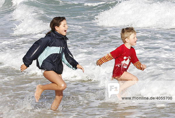 Girl  8 years  and boy  4 years  jumping and running in the waves on the beach of Fuerteventura  Canary Island  Spain  Europe