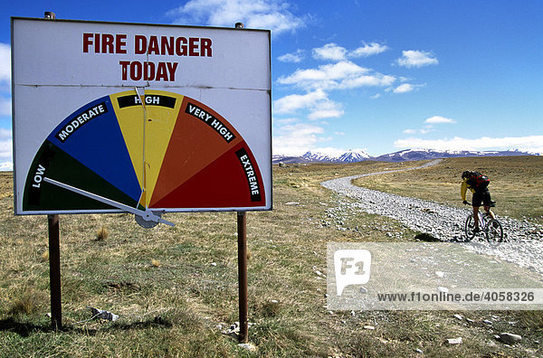 Mountainbiker riding past a Fire Danger sign  Lindis Pass  South Island  New Zealand