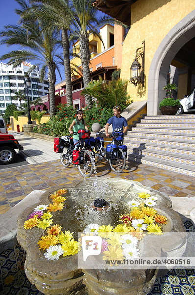 Bicyclists  fountain with blossoms in front of hotel in Las Americas  Tenerife  Canary Islands  Spain  Europe