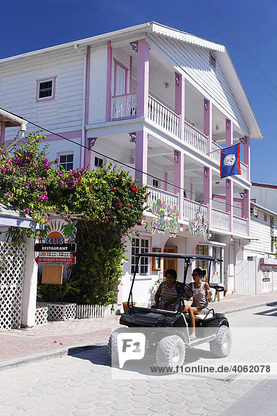 Golfcart mit zwei Frauen vor Holzhaus in karibischen Farben San Pedro Insel Ambergris Cay Belize Zentralamerika Karibik Holzhaus
