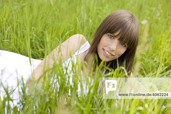 Junge dunkelhaarige Frau mit weißem Kleid genießt auf einer grünen Wiese liegend den Sommer