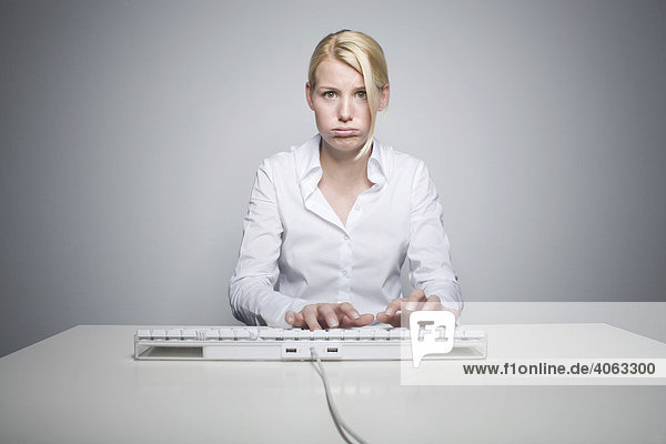 Junge blonde Frau tippt gestresst auf einer Computertatstaur