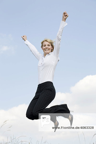 Young blonde woman wearing business clothing jumping in front of a blue sky  outstretched arms