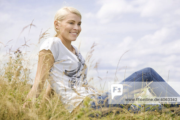 Junge blonde Frau sitzt im hohen Gras