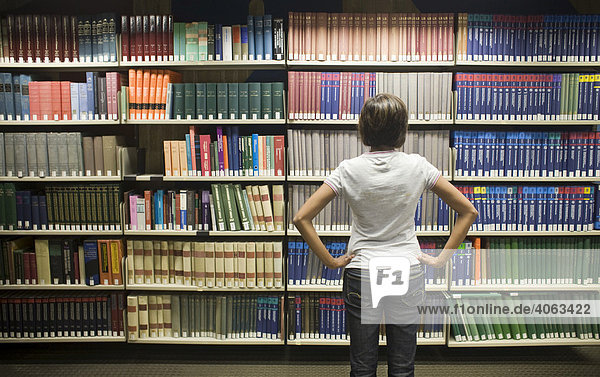 Junge dunkelhaarige Frau  Studentin  steht vor einem Bücherregal in einer Bibliothek