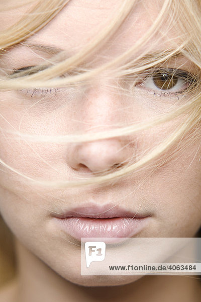 Young blond woman  hair partly covering her face  facial close-up