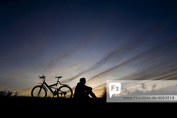 Junge Frau fährt Fahrrad  Mountain Bike  als Silhouette vor Abendhimmel