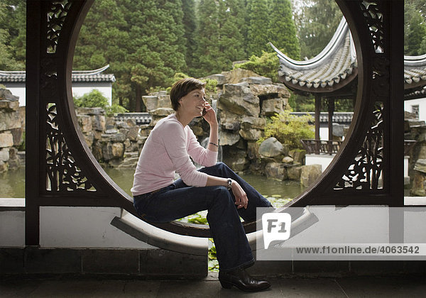 Junge Frau  Studentin telefoniert in einem chinesischen Garten mit einem Mobiltelefon