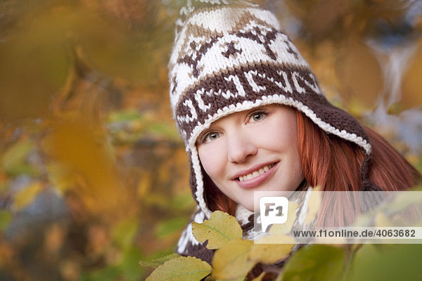 Young red haired woman wearing a woolen hat and scarf in an autumnal forest