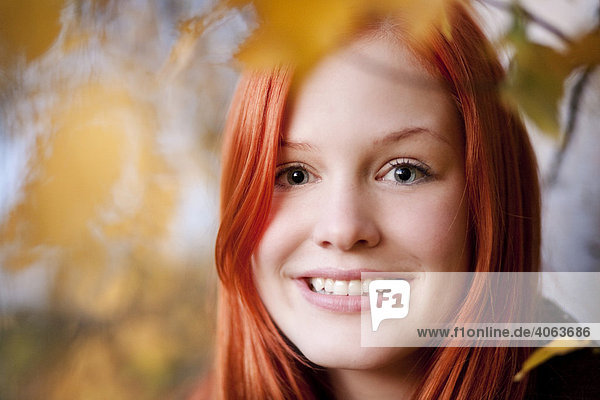 Portrait einer jungen rothaarigen Frau zwischen herbstlich gefärbten Blättern im Wald