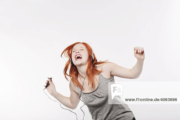 Junge Frau mit langen roten Haaren hört Musik über Kopfhörer