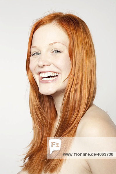 Portrait of a friendly laughing  young  red-haired woman in front of white backdrop