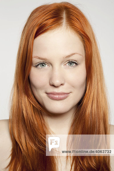 Portrait of a friendly smiling  young  red-haired woman in front of white backdrop