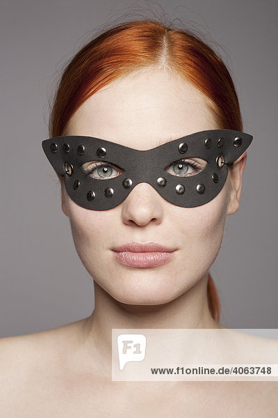 Young red-haired woman wearing a black leather mask