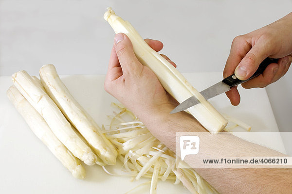 A chef peeling a white asparagus with a knife
