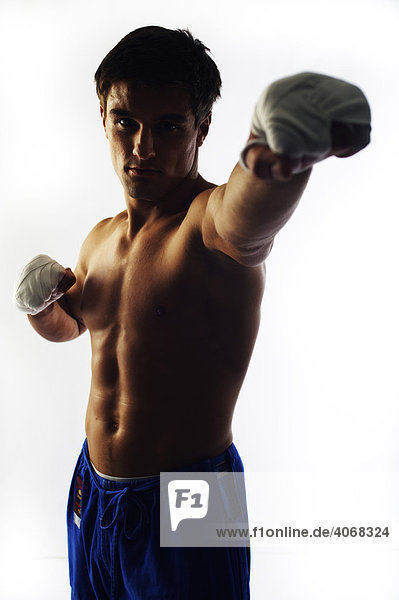 Young fighter with bare upper body and bandaged hands punching toward the camera  backlight