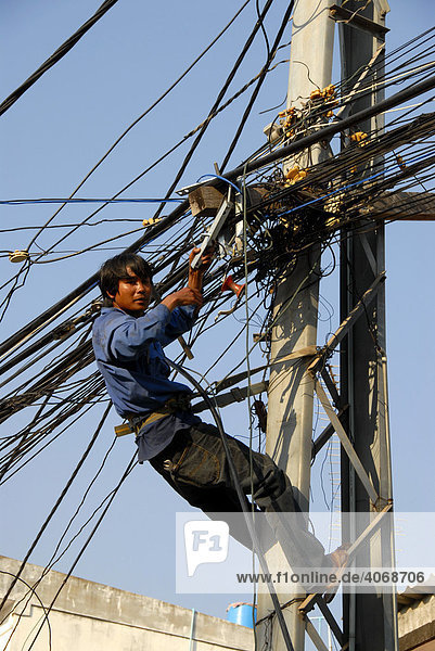 Elektrifizierung ohne Arbeitsschutz  Elekriker hängt im Gewirr von Stromkabeln  Vientiane  Laos  Asien