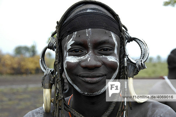 Portrait of a smiling young man from the Mursi tribe  wild  heavy headdress made of teeth of a male boar  near Jinka  Ethiopia  Africa