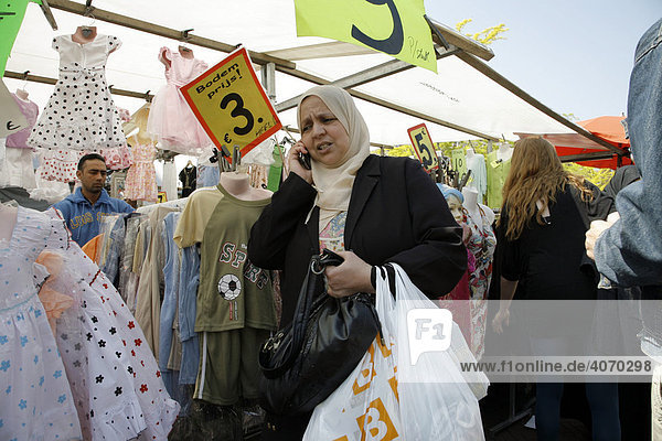 Woman wearing a headscarf talking on her cellphone next to a clothing stall at the Dappermarkt  a multicultural street market or bazaar in Dapperstraat  Amsterdam  Netherlands  Europe