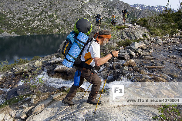 Hiker with backpack crossing a creek  Long Lake behind  Chilkoot Trail  Chilkoot Pass  British Columbia  B.C.  Canada  North America