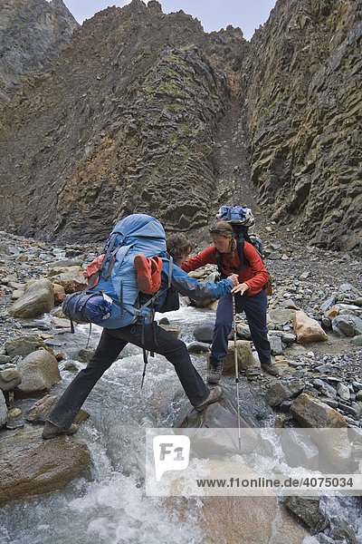 Zwei Wanderer  Rucksacktouristen  Frauen  helfen sich bei der Überquerung eines Baches  Donjek Route  St Elias Gebirge  Kluane Nationalpark  Yukon  Kanada  Nordamerika