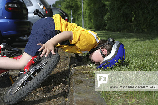 Five-year-old boy wearing a bicycle helmet falling off his bicycle,  posed photo