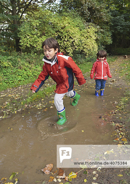 Children wearing rubber boots walking through puddles  Niederwerth  Rhineland-Palatinate  Germany  Europe