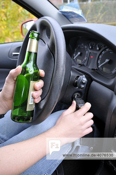 Hände eines Autofahrers mit Bierflasche am Steuer