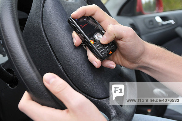 Hand eines Autofahrers schreibt SMS am Steuer