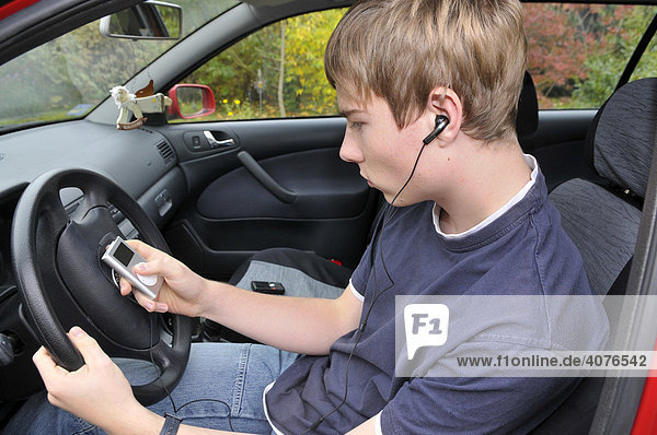 Jugendlicher hört mit Kopfhörern Musik am Steuer eines Autos