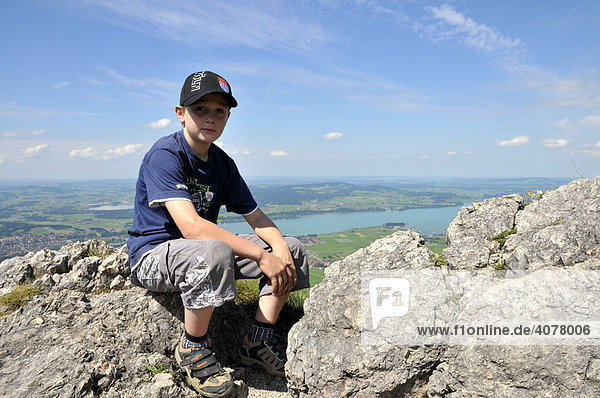 Ein achtjähriger Junge macht Rast  Tegelberg  hinten der Forggensee  Allgäuer Alpen  Bayern  Deutschland  Europa