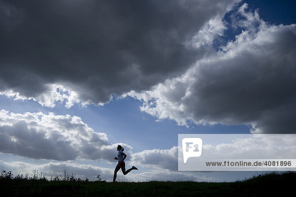 Running woman as a silhouette in front of a sky with dark clouds