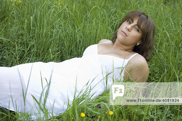 Frau liegt mit weißem Kleid im hohen Gras auf einer Wiese
