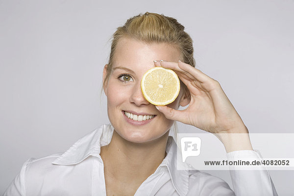 Junge Frau hält sich eine Zitronenscheibe vor ein Auge