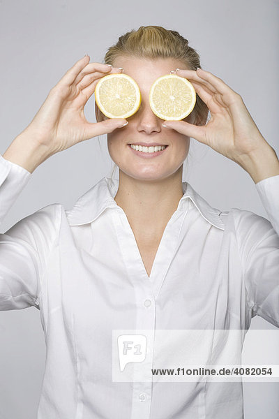 Junge Frau hält sich zwei Zitronenscheiben vor die Augen