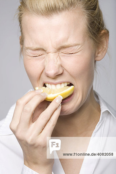Junge Frau beißt in eine Zitrone und macht ein komisches Gesicht