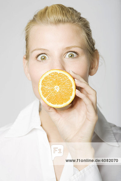 Blonde Frau hält sich eine aufgeschnittene Orange vor den Mund