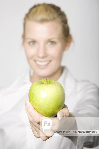 Junge blonde Frau hält einen grünen Apfel in Richtung Kamera