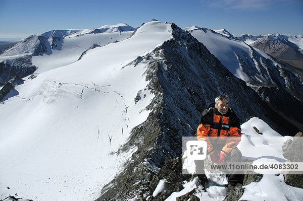 Mountaineer sits on rocks in front of a snow covered mountain Kharkhiraa Mongolian Altai near Ulaangom Uvs Aymag Mongolia
