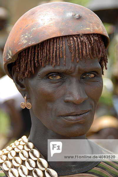 Portrait streng dreinblickende Frau mit Kette aus Kaurimuscheln und Kalabasse auf dem Kopf auf dem Markt von Keyafer Äthiopien