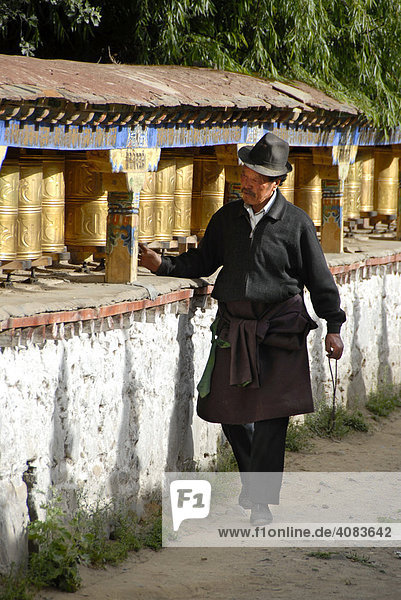 Tibetan pilgrim turns golden prayer wheels of a mani wall Samye Monastery Tibet China