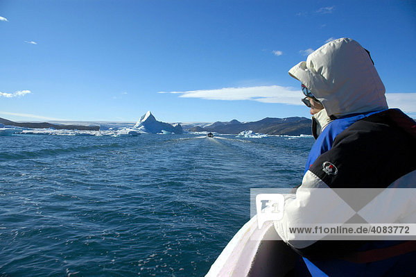 Warm dressed person watches the Arctic Sea with icebergs out of an open motorboat Sermilik Fjord Eastgreenland