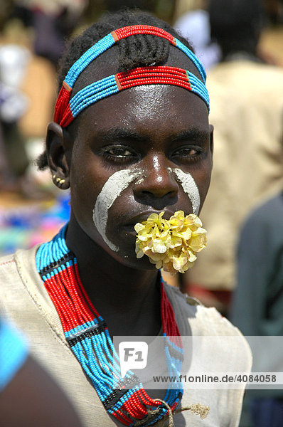 Young man with a flower in his mouth and colourful necklace and head adorments market of Keyafer Ethiopia